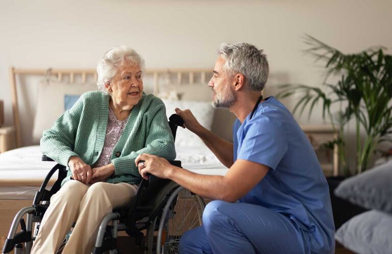 A caregiver and elderly woman smiling together while looking at a notebook in a cozy living room.